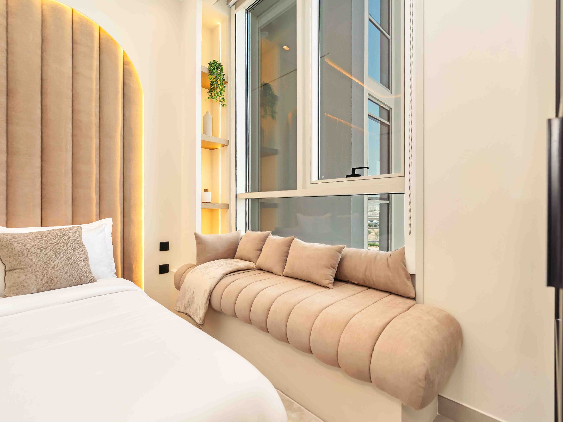 Bedroom with arched fluted upholstered headboard, recessed shelving niche and built-in window bench