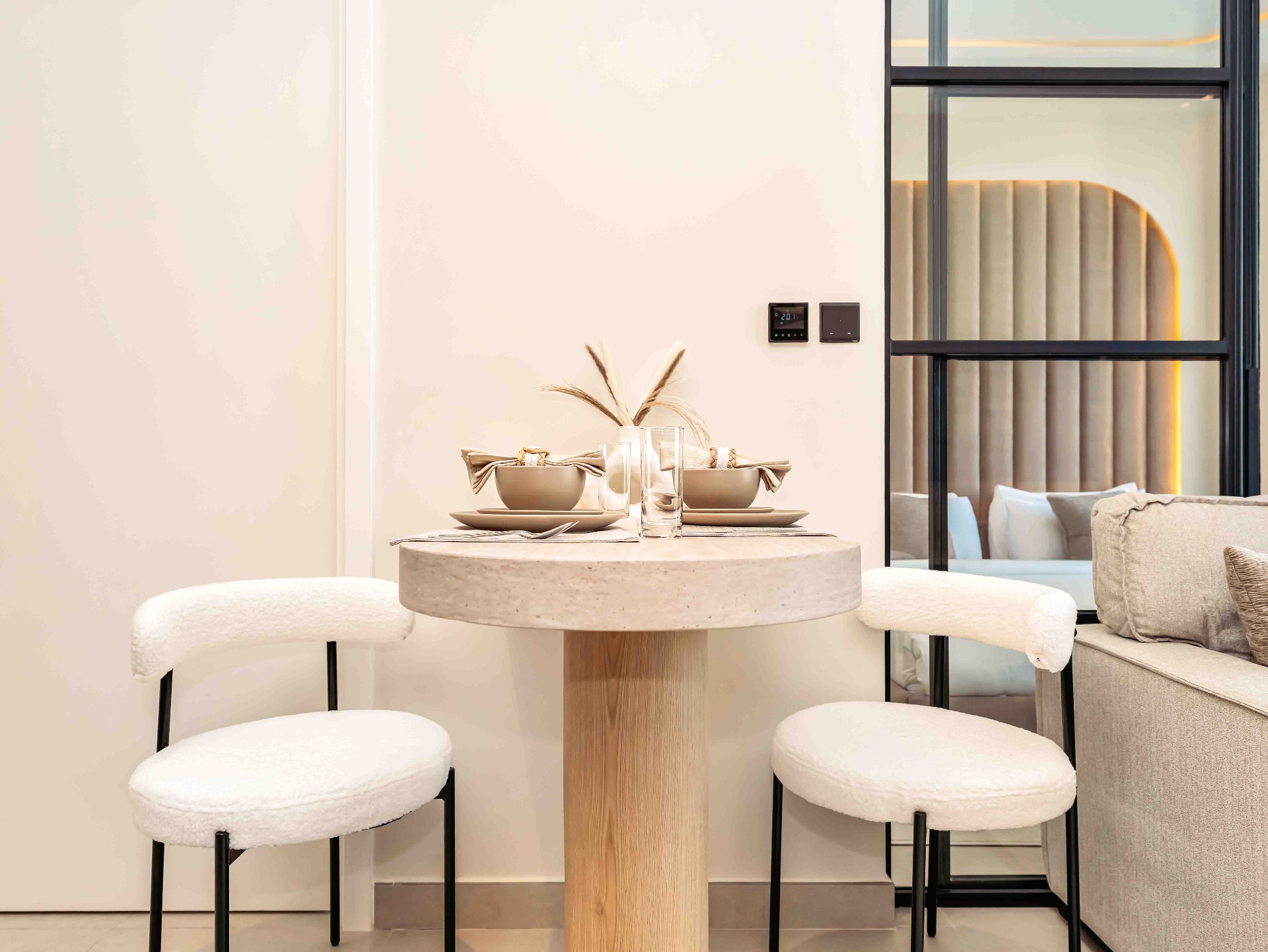 Travertine pedestal dining table with boucle chairs and steel-framed glass partition