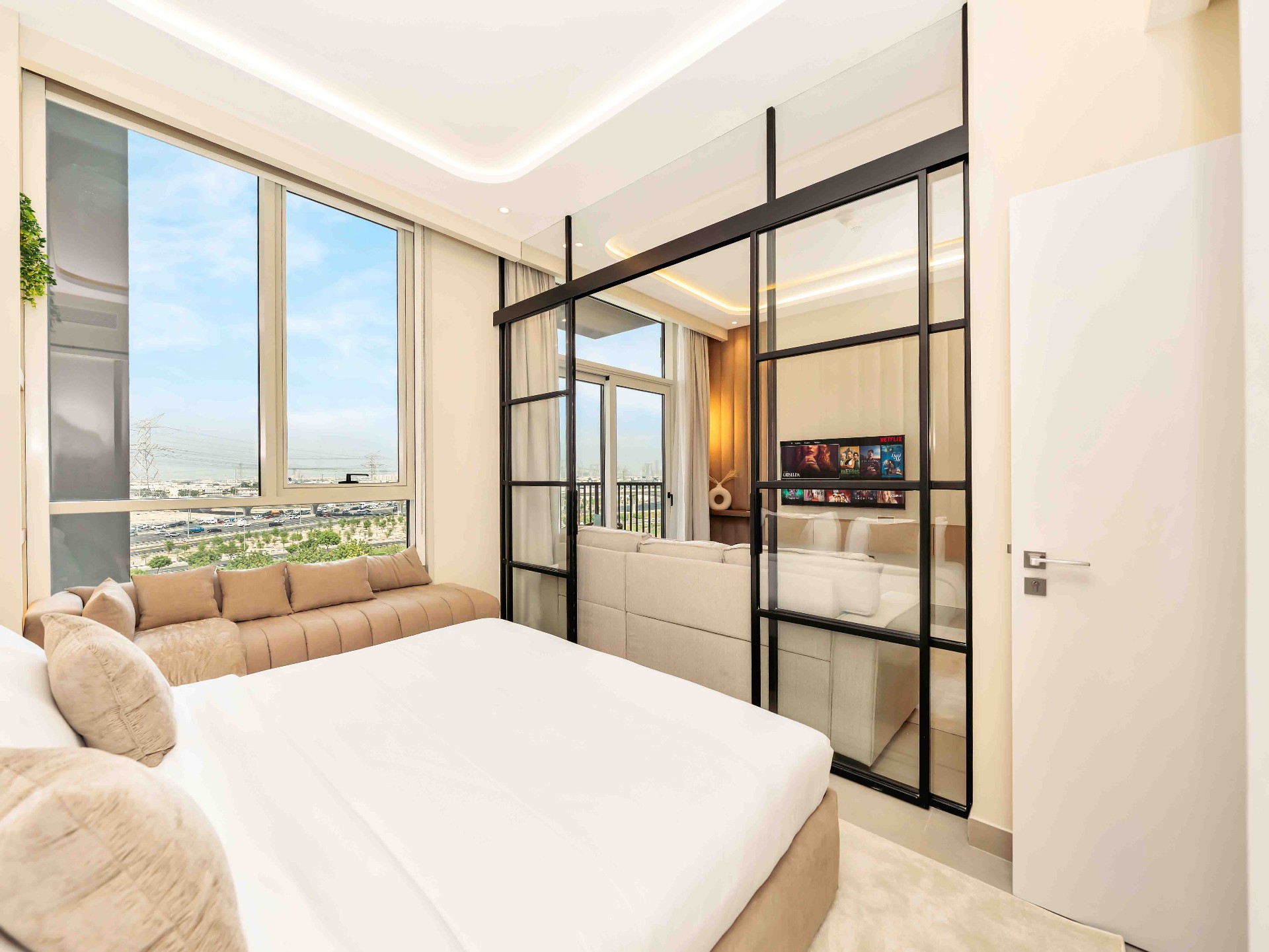 Bedroom view through steel-framed mirrored partition out to living room and balcony