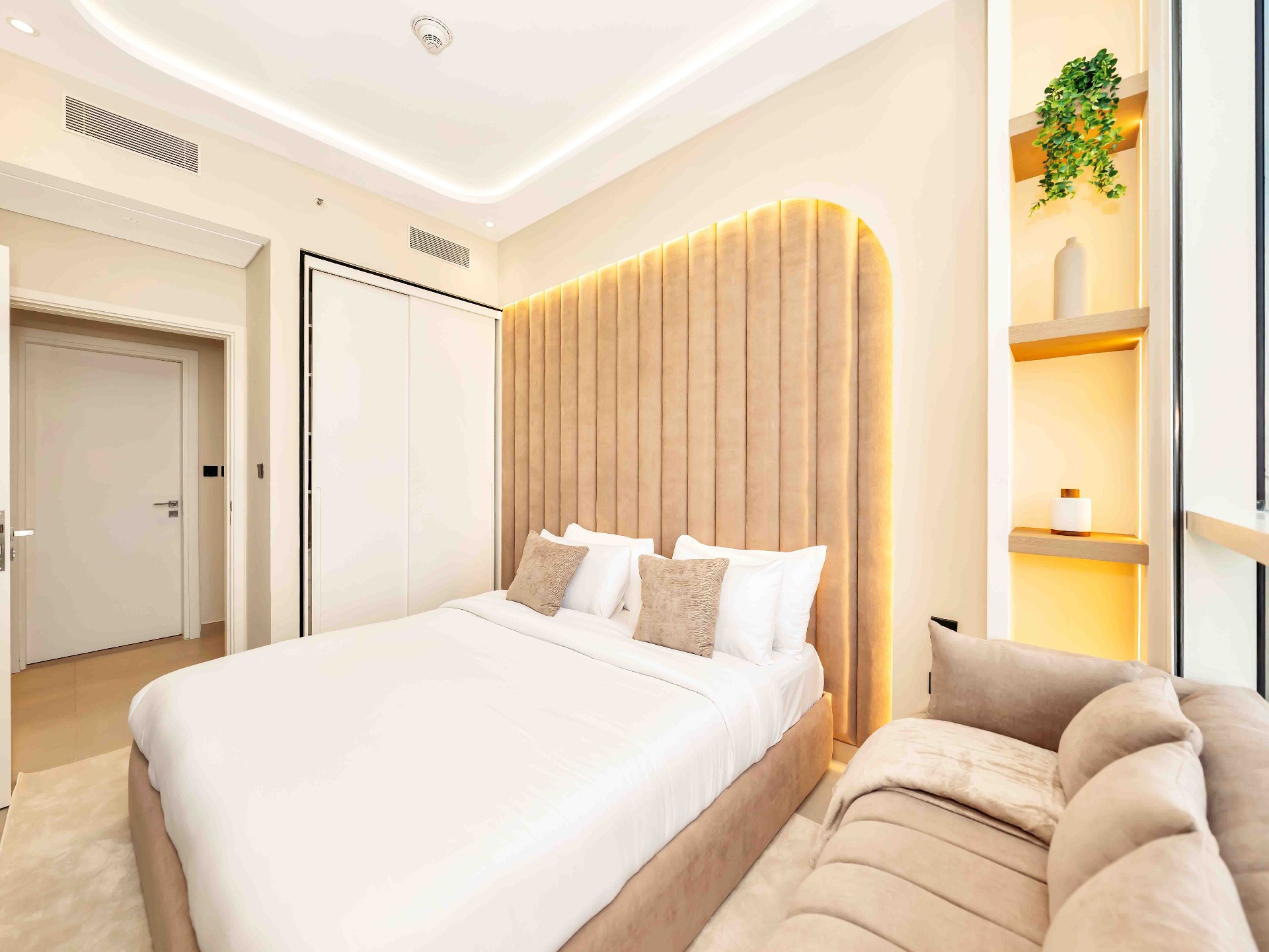 Master bedroom with full-height arched fluted headboard, warm cove lighting and shelving niche