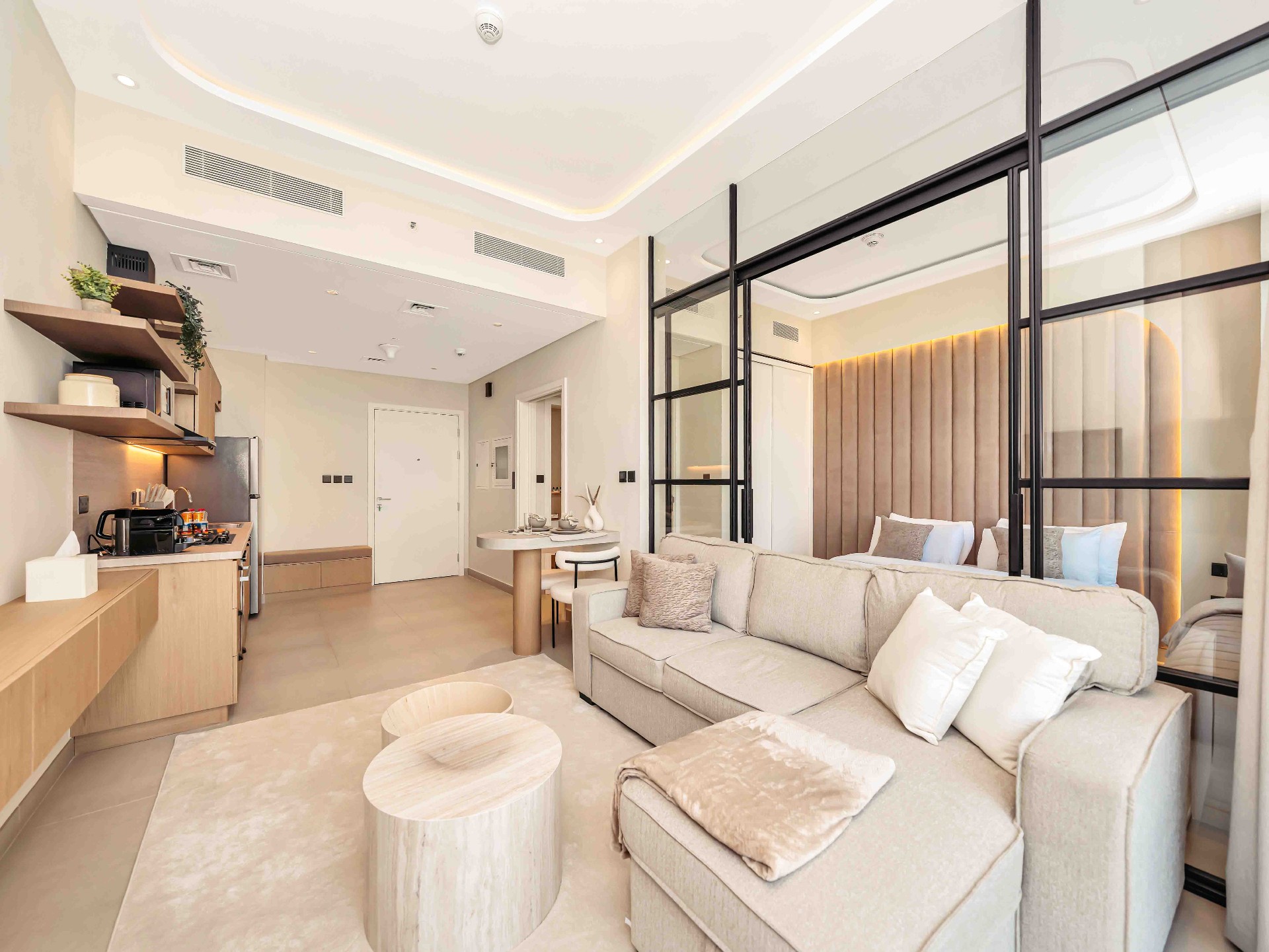 Living area with steel-framed mirrored partition revealing bedroom and warm oak joinery