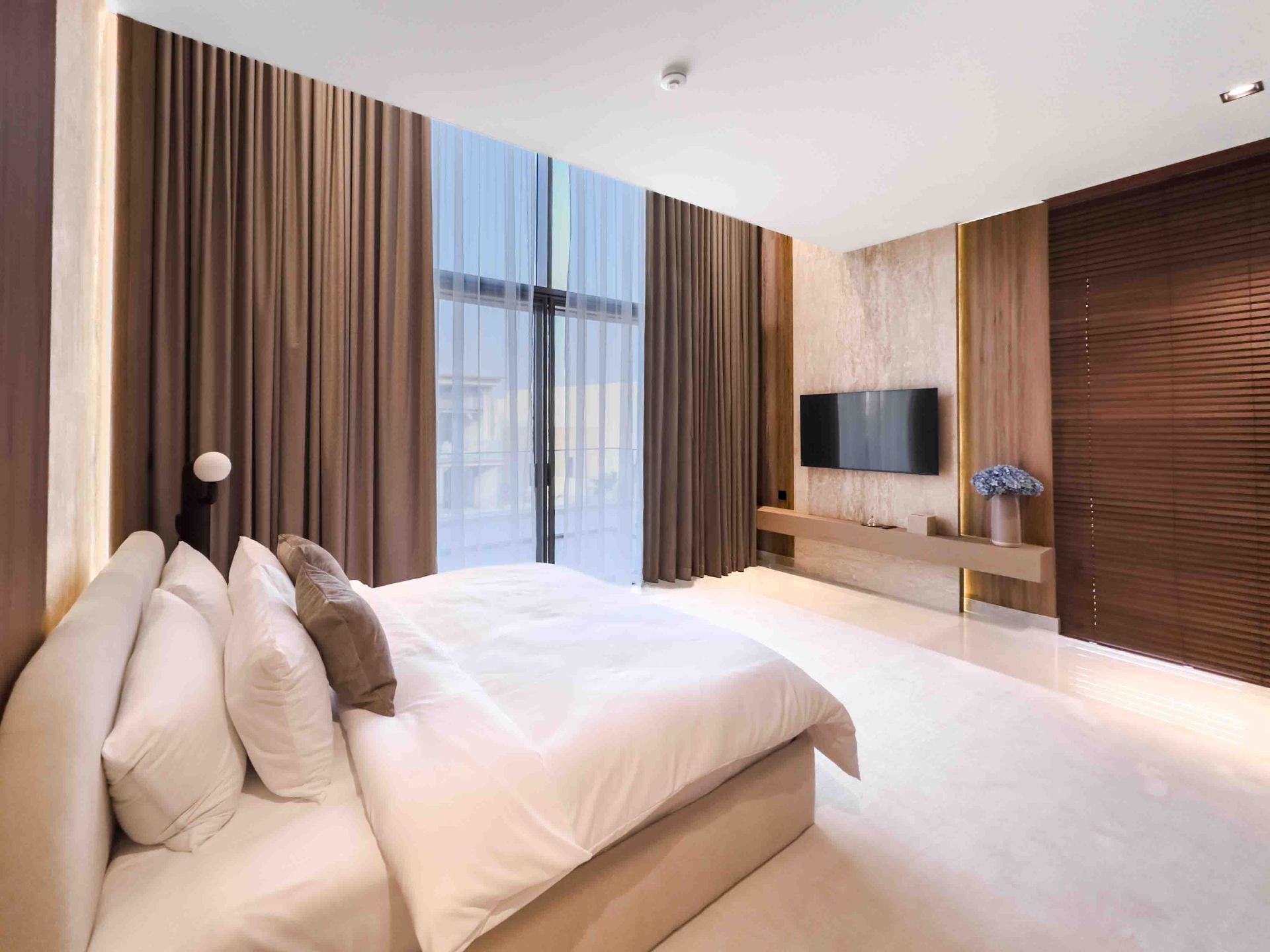 Bedroom with travertine TV wall, oak floating console and full-height curtains