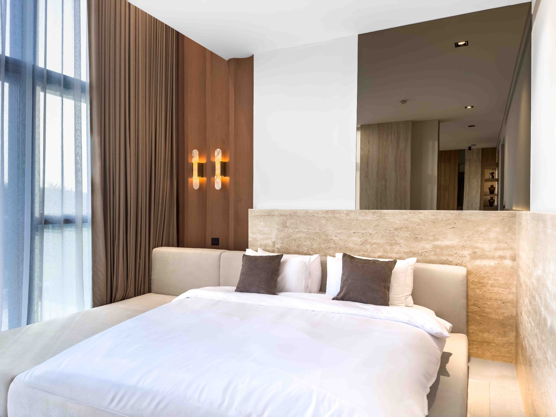 Bedroom with travertine headboard wall, oak panelling and alabaster sconces