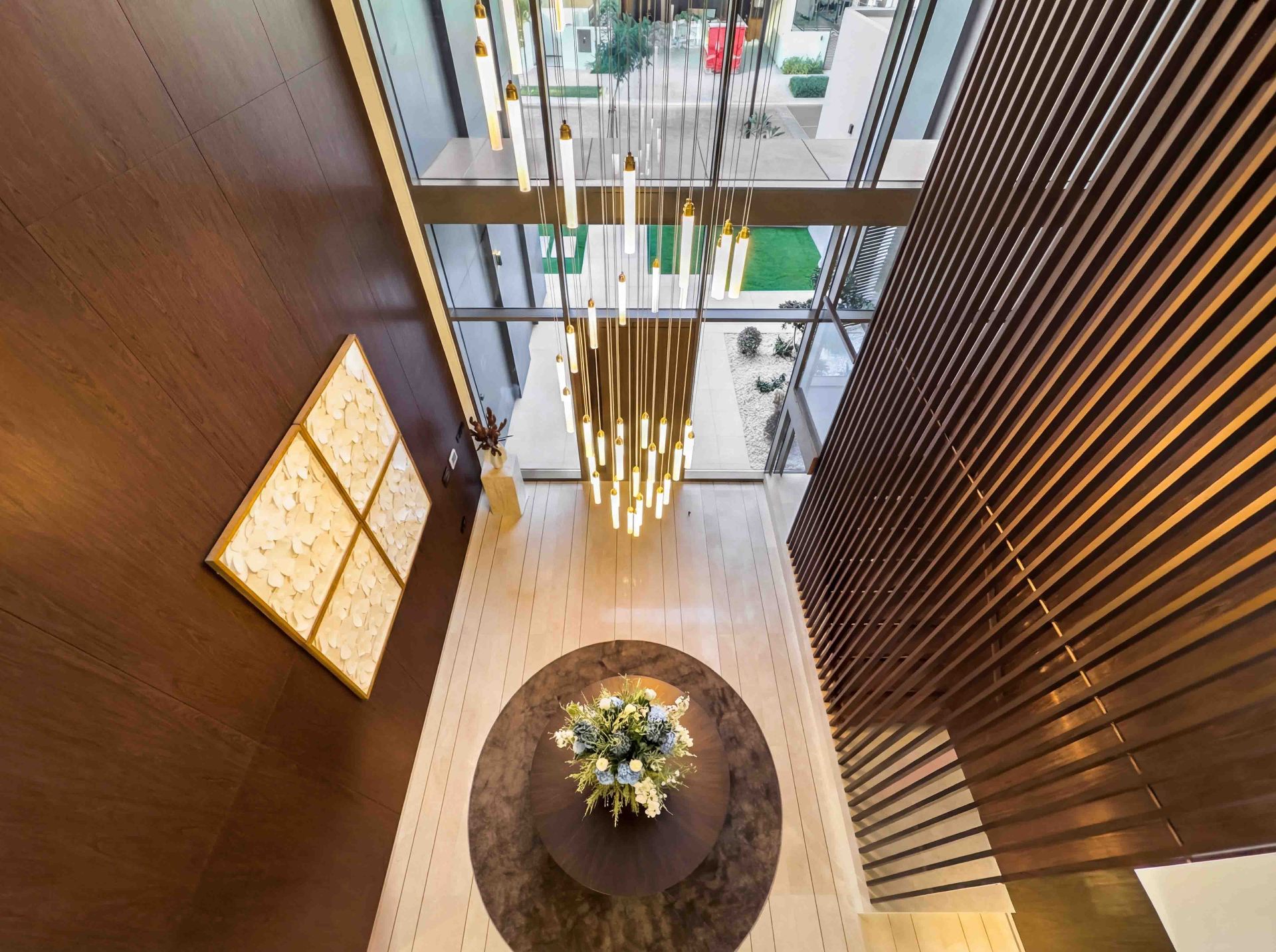 Double-height entrance hall with cascading pendant chandelier and timber slat screen