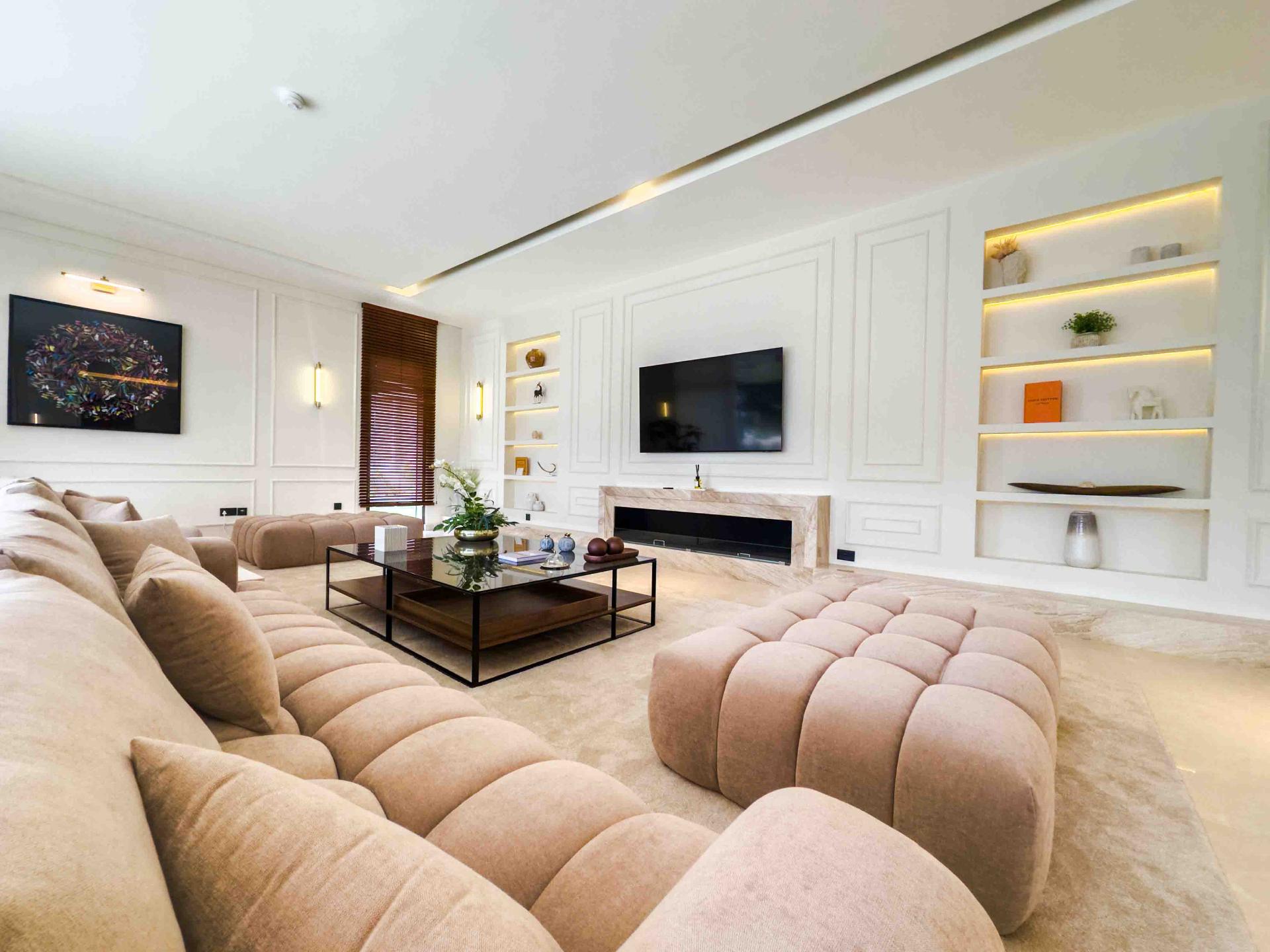 Living room with tufted modular sofa, panelled feature wall and integrated shelf lighting