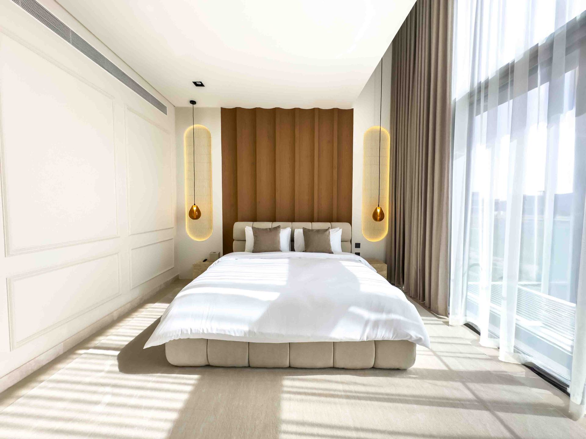 Bedroom with fluted oak headboard wall, alabaster pendants and floor-to-ceiling sheers