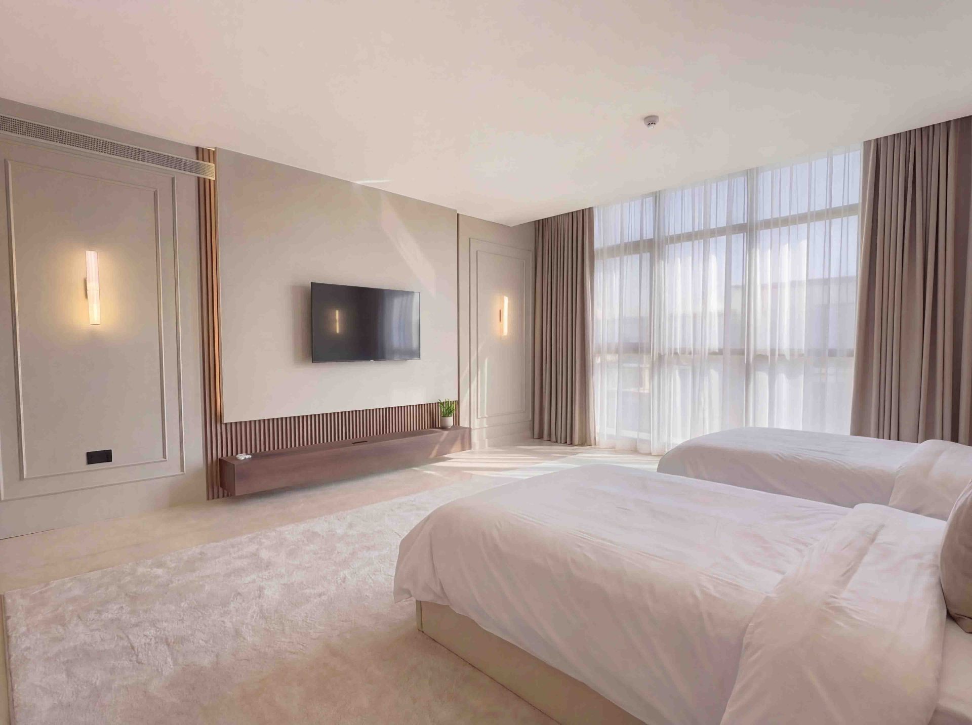 Twin bedroom with floating timber TV console, panelled walls and full-height sheers