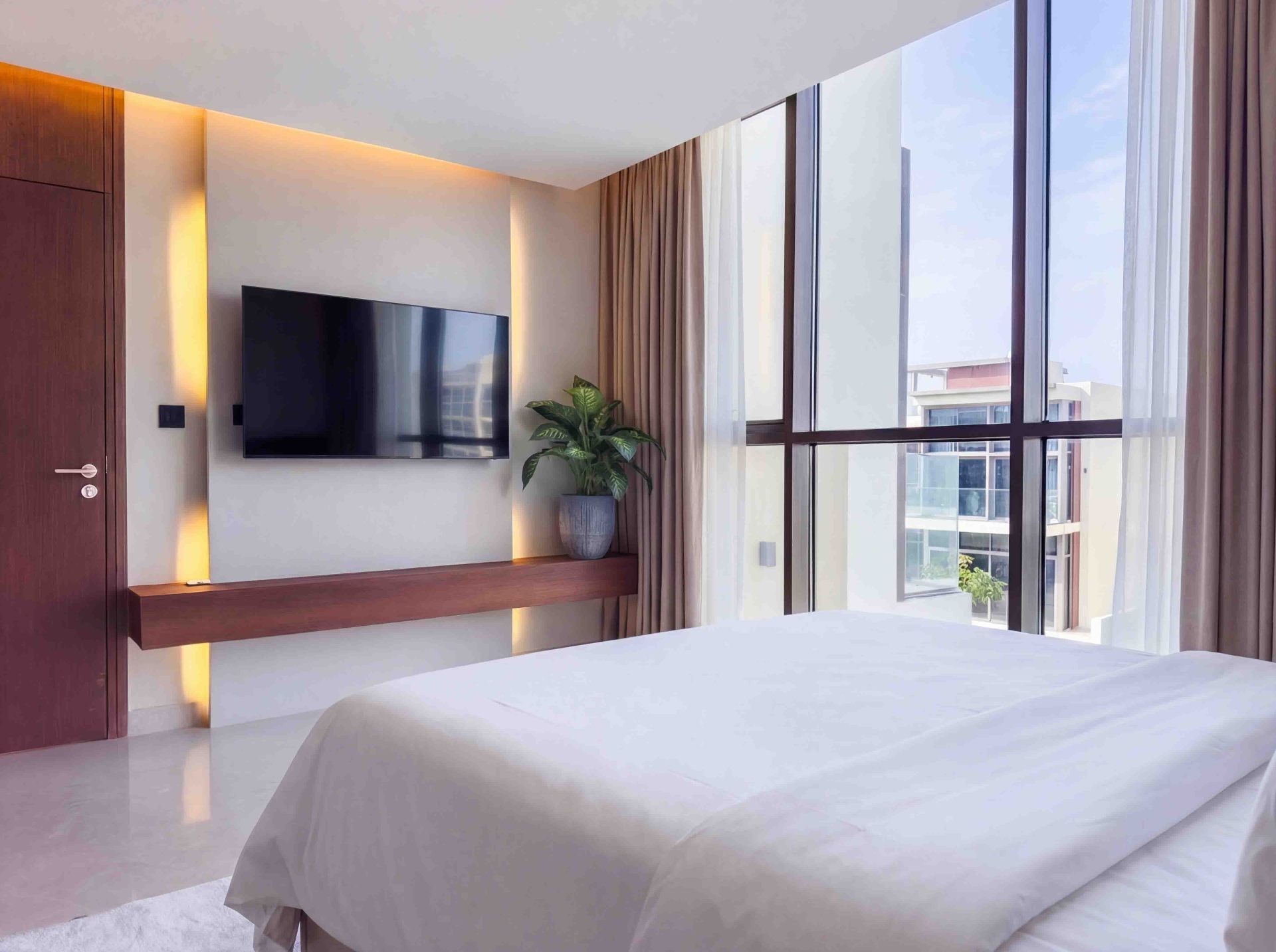 Bedroom with floating walnut TV shelf, cove lighting and full-height window