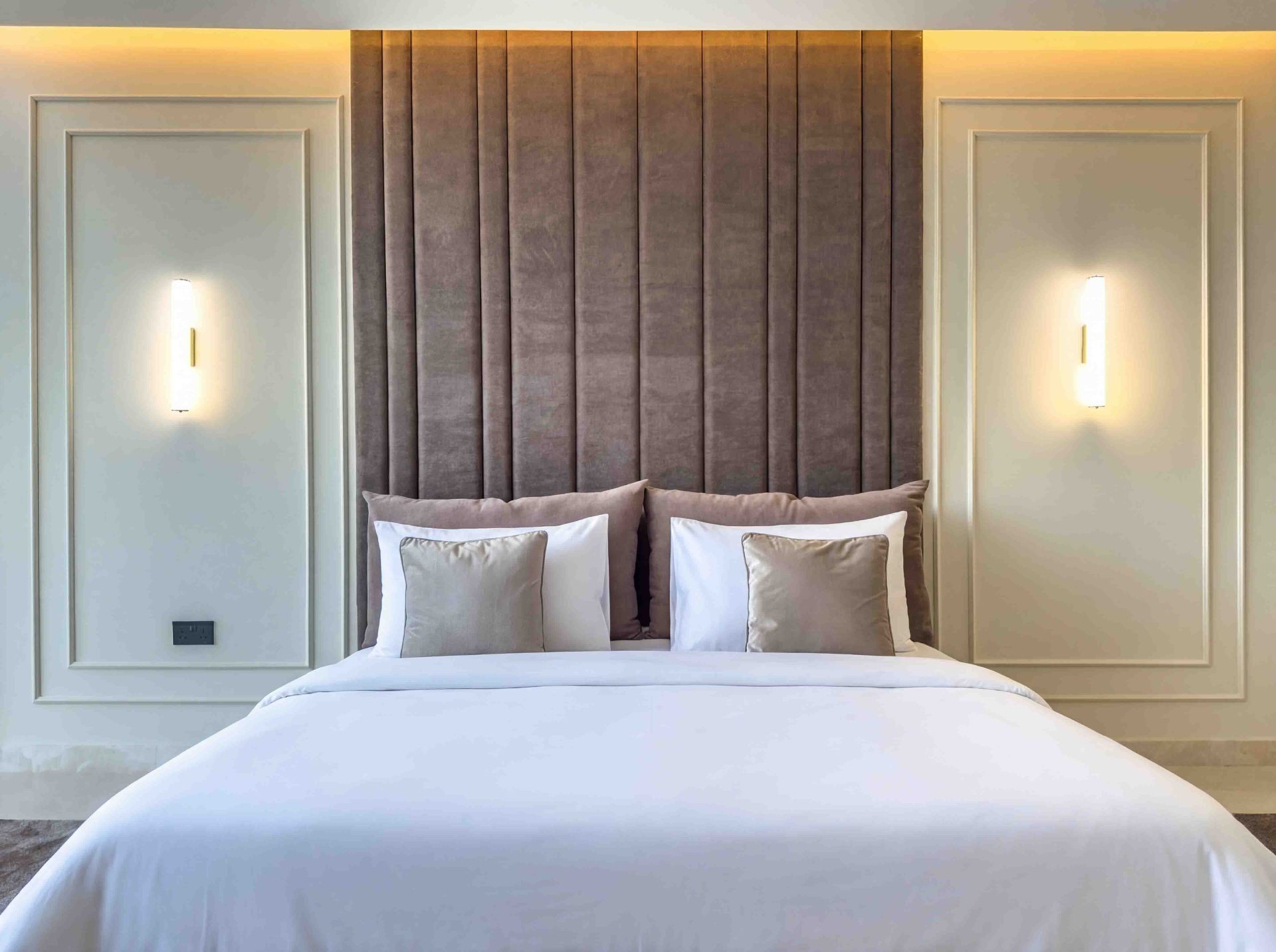 Bedroom with vertical velvet headboard panels, cove lighting and brass sconces