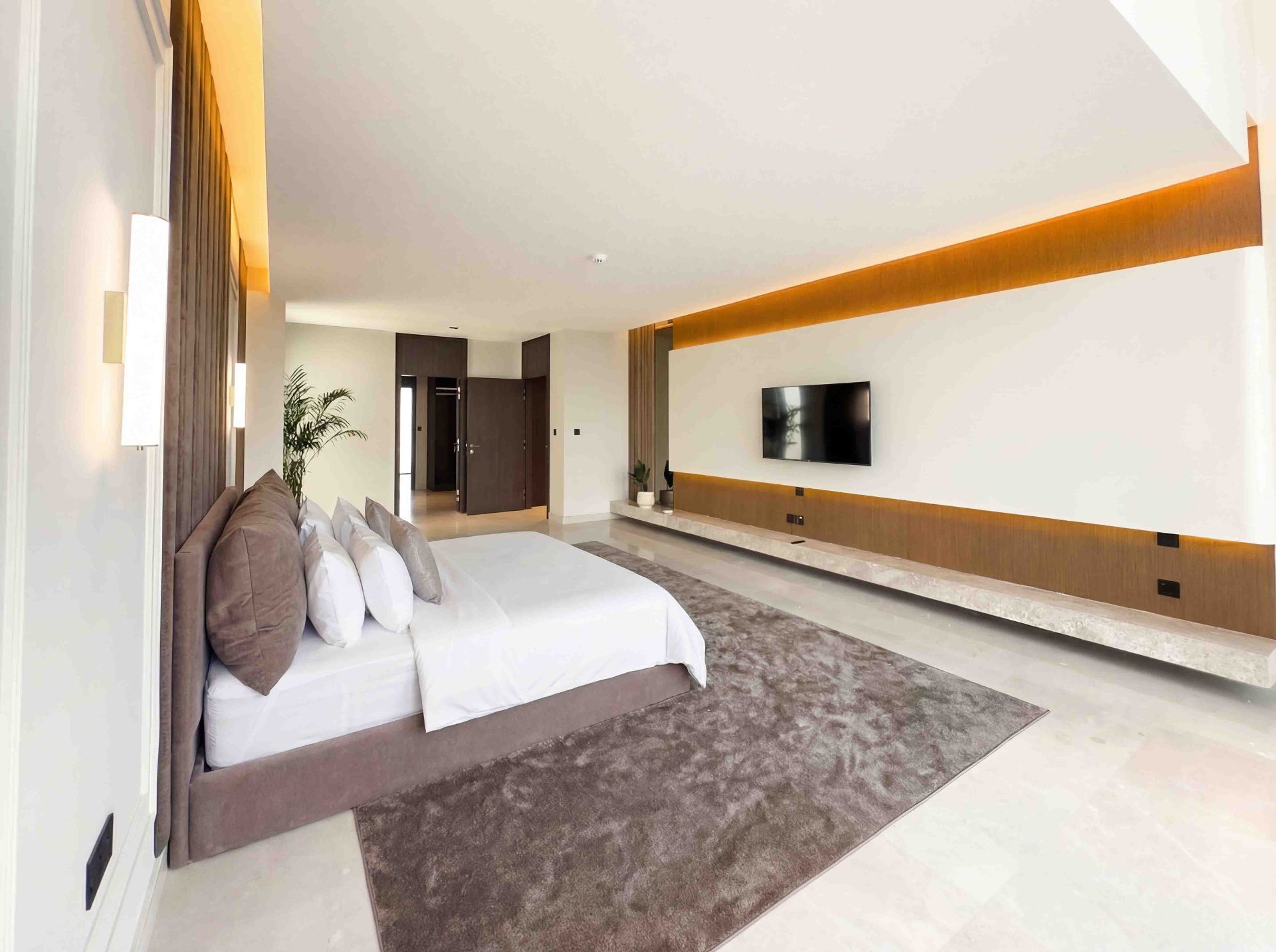Primary suite with floating travertine TV plinth, warm cove lighting and timber panelling