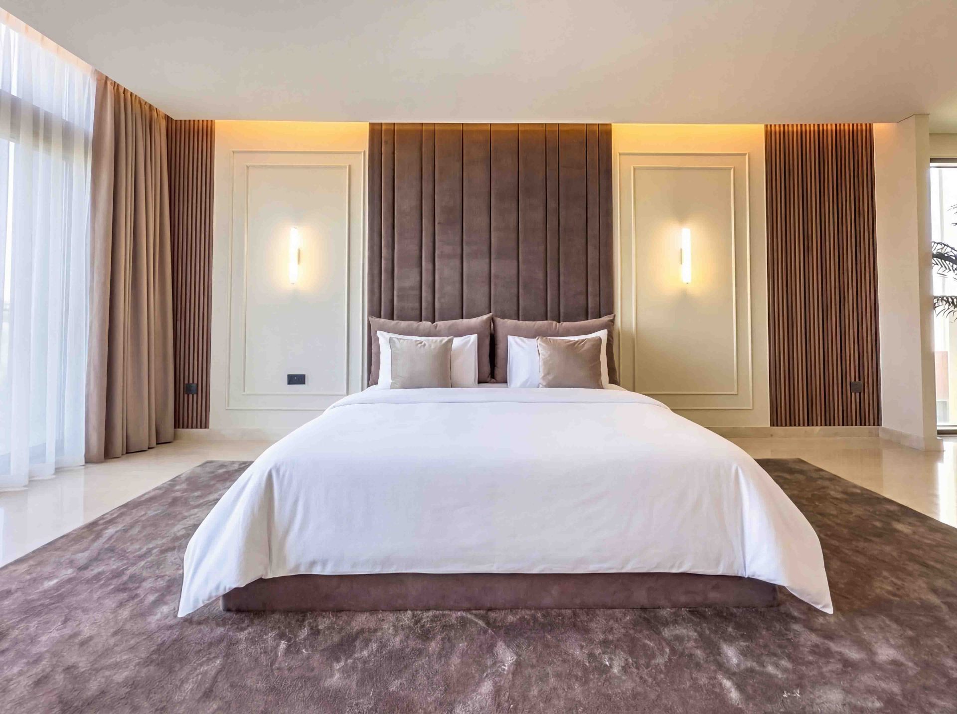 Primary bedroom with velvet panelled headboard wall, brass sconces and plush rug