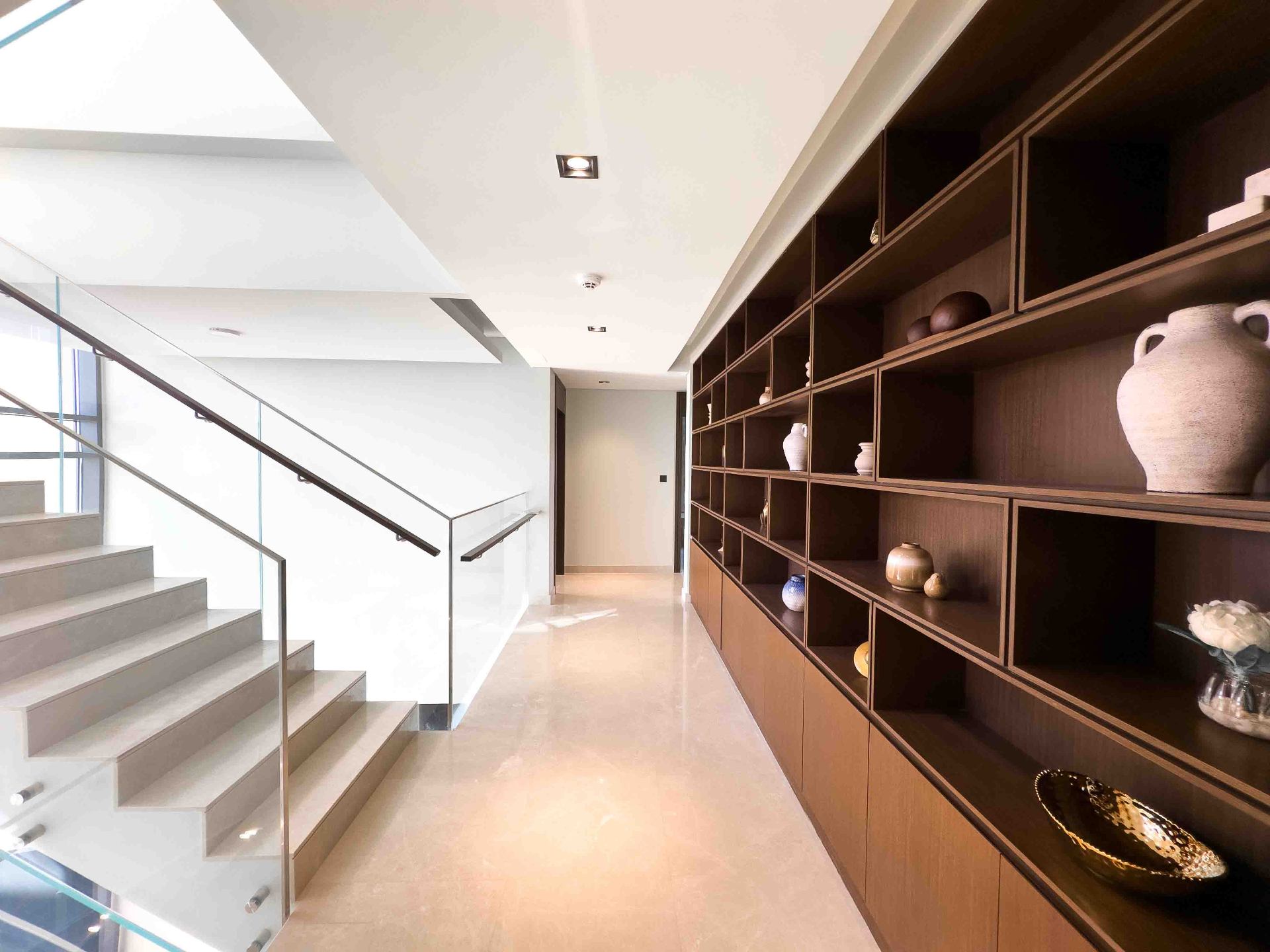 Upper hallway with floor-to-ceiling walnut display shelving and glass-railed staircase