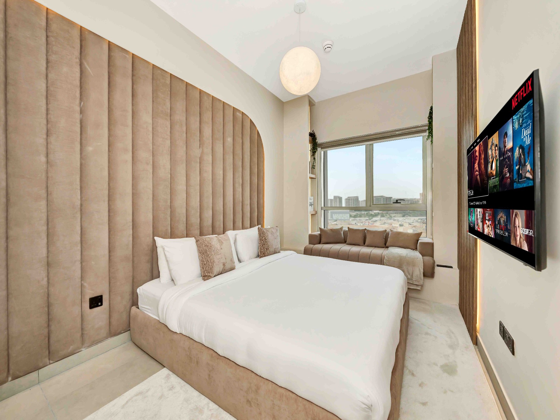 Bedroom with arched fluted velvet headboard, upholstered window daybed and wall-mounted TV on fluted oak panel