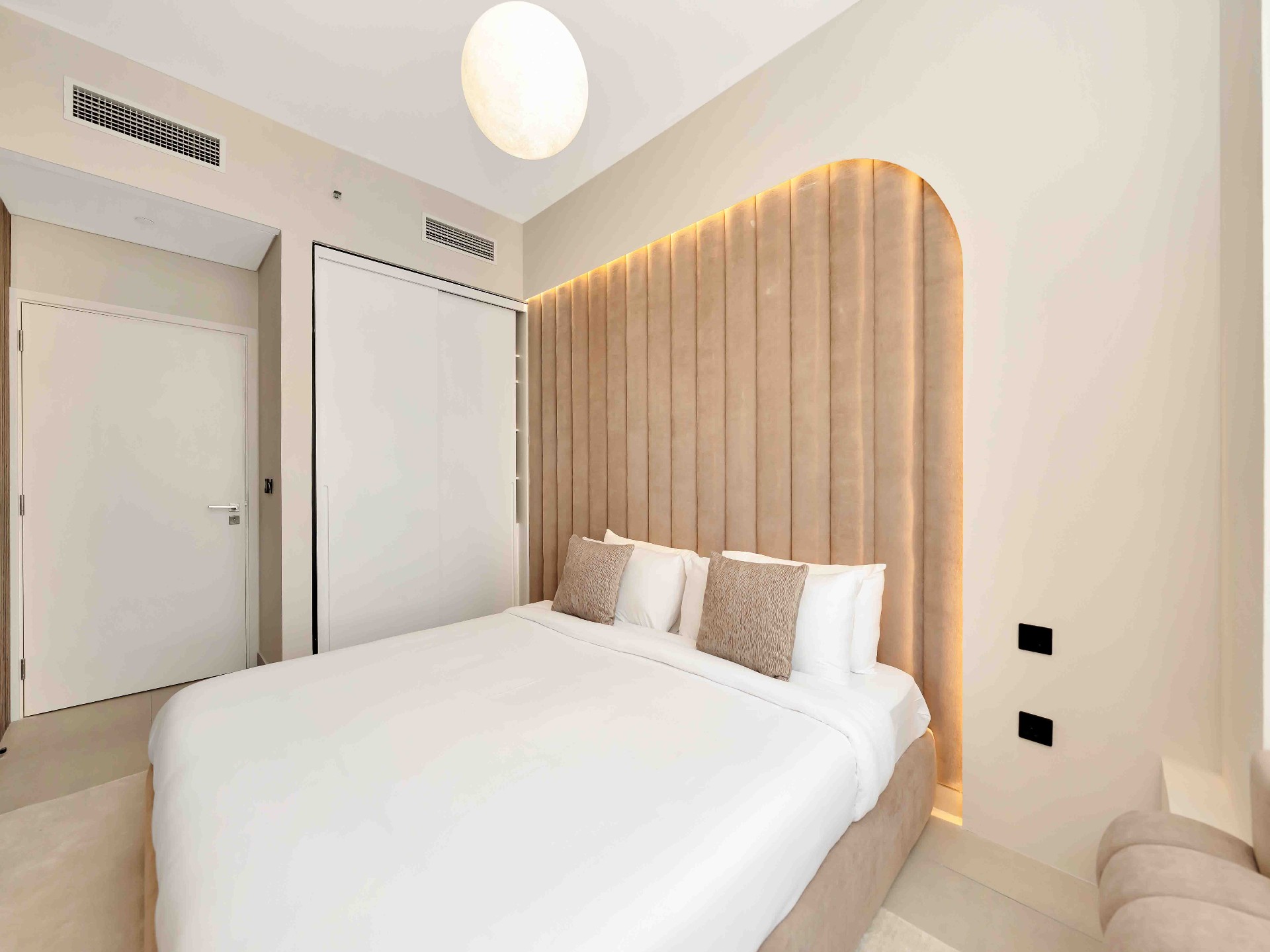 Bedroom with full-height arched fluted headboard, warm cove lighting and white sliding wardrobe