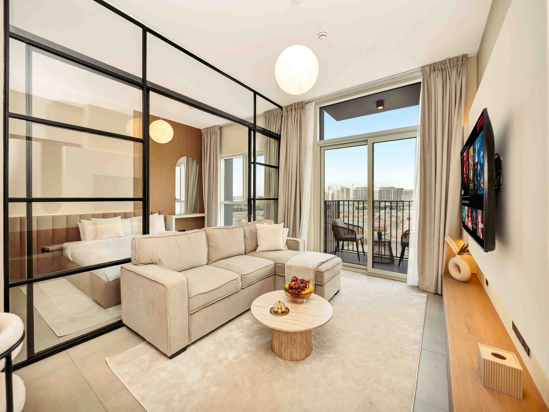 Open-plan living and bedroom with steel-framed glass partition, floating oak TV console and balcony