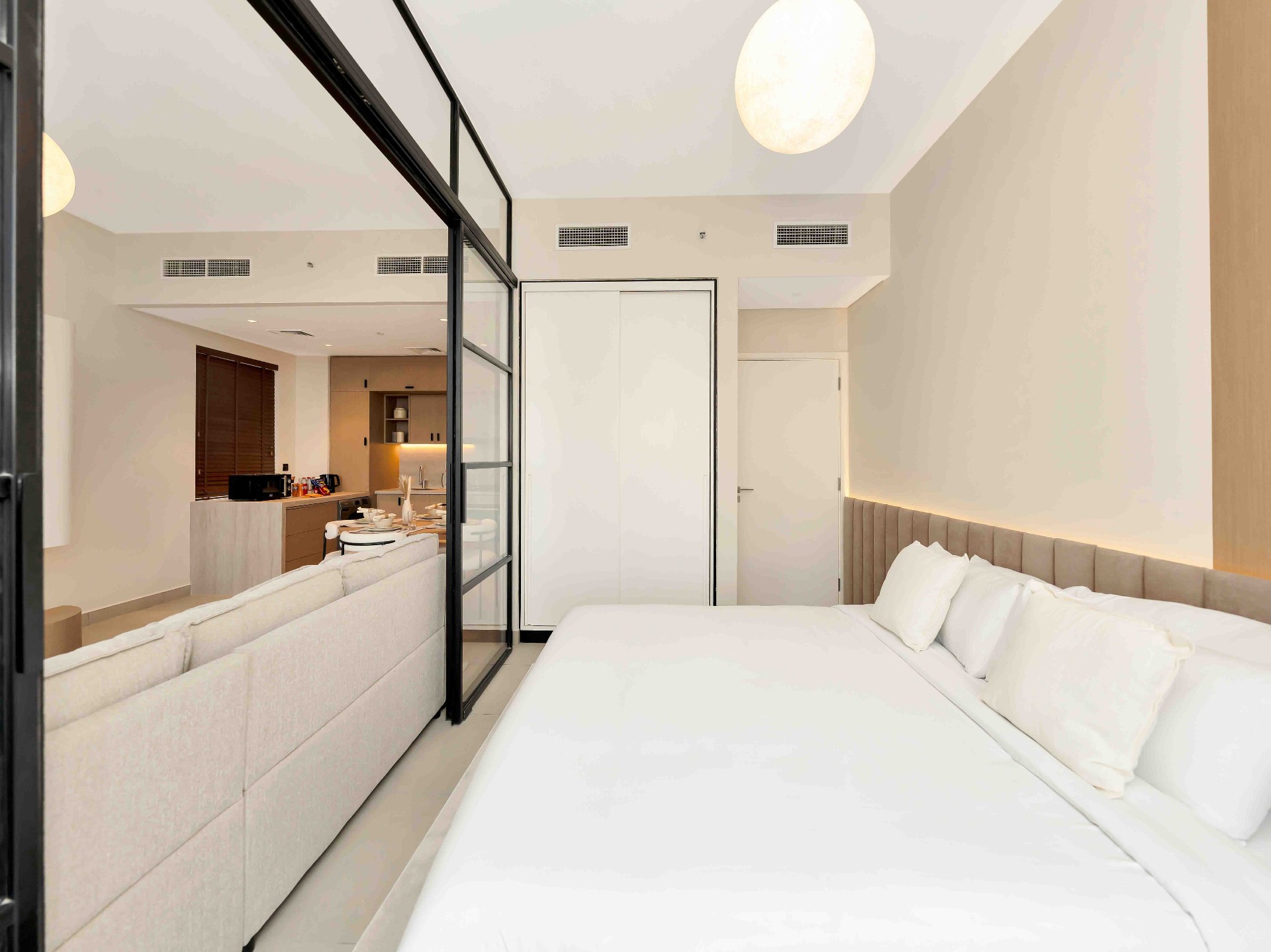 Bedroom with steel-framed glass partition opening to living and kitchen area